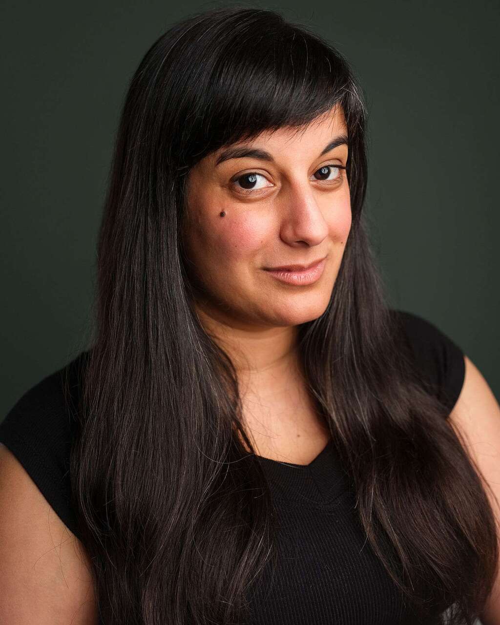 Michelle Kelly, a brown skinned mixed race woman with long dark hair, looks at the camera and smiles.